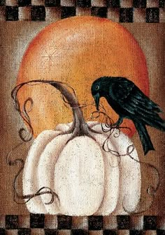 a black bird sitting on top of a white pumpkin next to an orange and black flag