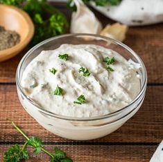 a glass bowl filled with white sauce and parsley on top of a wooden table