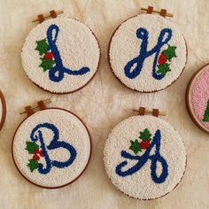 four embroidered christmas monograms with scissors and holly on them, sitting next to each other