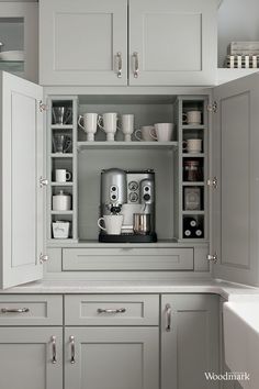 a coffee maker is in the corner of a kitchen cabinet with cups and mugs on it