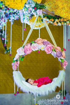 a baby in a pink dress is laying on a white swing with flowers and feathers