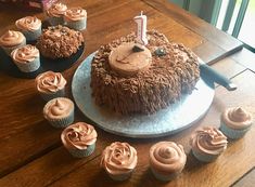 a birthday cake with chocolate frosting and cupcakes on a table next to it