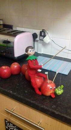 an elf is sitting on top of apples and carrots in front of a toaster