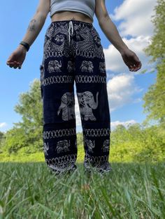 a woman standing in the grass with her hands out and wearing elephant print pants on