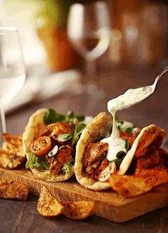 some tacos and chips are on a wooden board with a glass of wine in the background