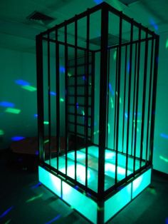 a cage that is lit up with blue and green lights in the dark, it appears to be an empty room