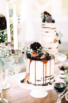 a wedding cake sitting on top of a wooden table next to two wine glasses and candles