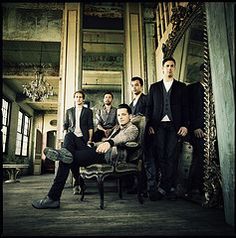 a group of men standing and sitting around each other in a room with chandeliers