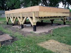 a large wooden structure sitting in the middle of a field next to a tree and grass area