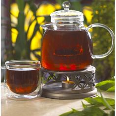 a glass tea pot filled with liquid sitting on top of a table next to a cup