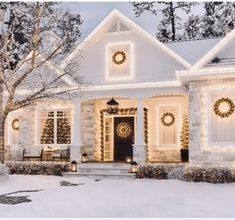 a white house with christmas lights and wreaths on it's front door in the snow