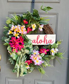 a wreath with flowers and the word aloha on it hanging on a door