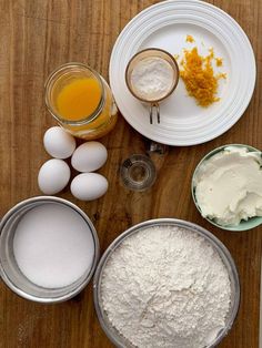 the ingredients to make an orange cake are displayed on a wooden table, including eggs and flour