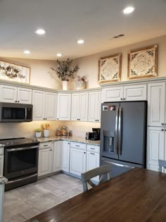 a kitchen with white cabinets and stainless steel appliances is pictured in this image, there are two pictures on the wall above the refrigerator