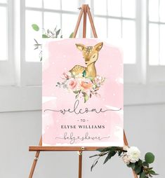 a pink welcome sign with a deer on it and flowers in the foreground is an easel