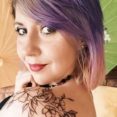 a woman with purple hair and tattoos on her chest holding an open umbrella over her shoulder