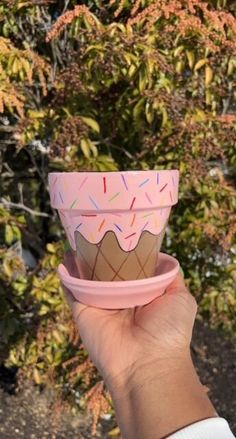 a hand holding up a cup that has sprinkles on it and is in front of some bushes