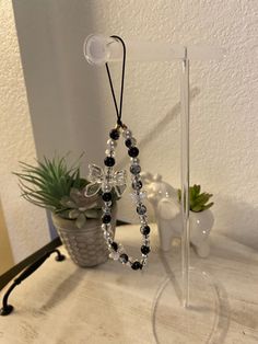 a cross is hanging from a clear stand on a white table next to a potted plant