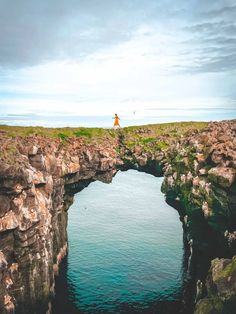 a person standing on the edge of a cliff over looking water and land with cliffs in the background