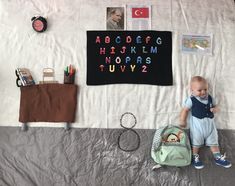 a baby standing next to a backpack and some school supplies on a sheeted wall