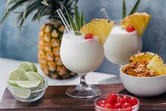 three glasses filled with different types of food on top of a wooden tray next to pineapples