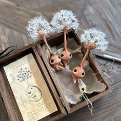 three little dolls in a wooden box with dandelions on them and an old paper