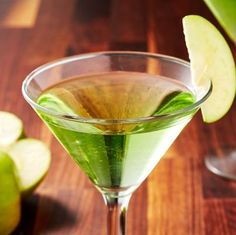 a green drink in a martini glass next to sliced apples