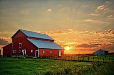 a red barn sitting on top of a lush green field under a cloudy sky at sunset