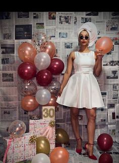 a woman in a white dress standing next to balloons and presents on a newspaper background