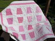 a pink and white quilt sitting on top of a wooden bench next to a fence