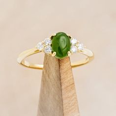 a close up of a ring on top of a wooden stand with a green stone in the middle