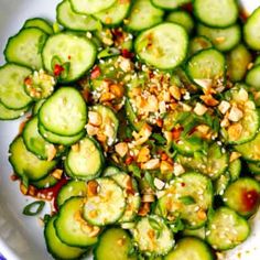 a white bowl filled with sliced cucumbers and nuts on top of a table