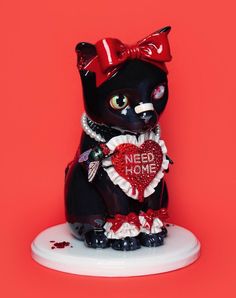 a black cat figurine with a red bow on its head holding a heart