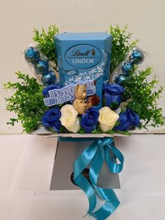 a bouquet of flowers and chocolates in a box with blue ribbon tied around it