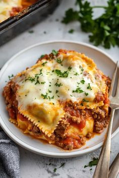 a white plate topped with lasagna covered in sauce and cheese next to a fork