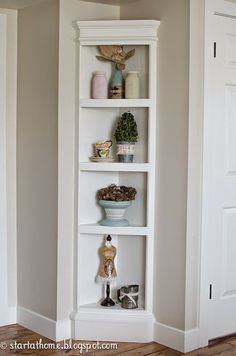 a tall white shelf with pots and plants on it in the corner of a room