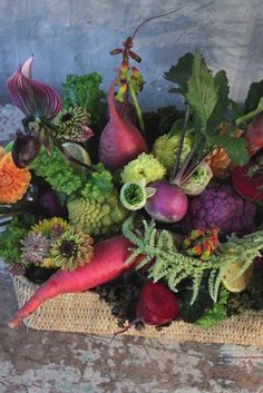 a bunch of vegetables that are sitting in a basket on the ground with leaves and flowers around them