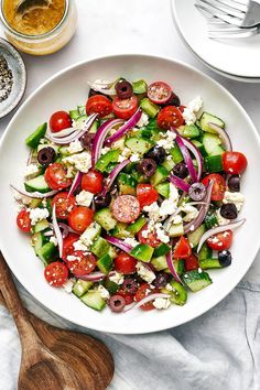 a salad with cucumbers, tomatoes, olives and feta cheese in a white bowl