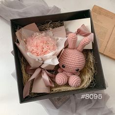 a pink crocheted bunny sitting in a box next to a flower and book