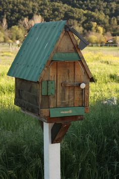 a wooden bird house sitting on top of a white pole in the middle of a field