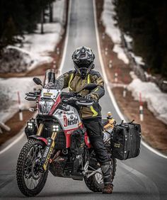 a man riding on the back of a motorcycle down a road next to snow covered trees