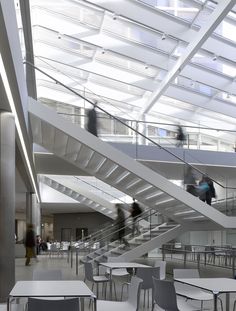 people are walking up and down the stairs in an open area with white tables and chairs