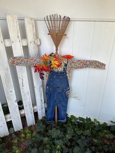 a scarecrow is hanging on the side of a white fence with flowers in it