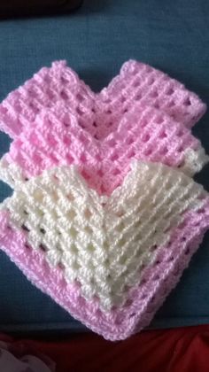 three crocheted baby blankets sitting on top of a blue cloth covered in white and pink yarn