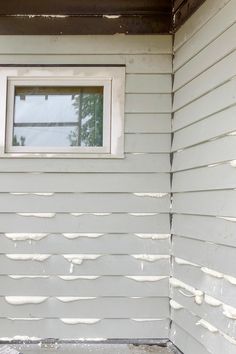 the side of a house with white paint on it and a window in the corner