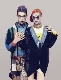 two people with makeup and body art standing next to each other in front of a gray background