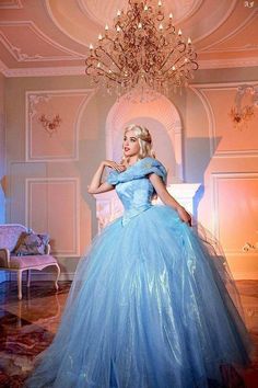 a woman in a blue ball gown posing for the camera with a chandelier behind her