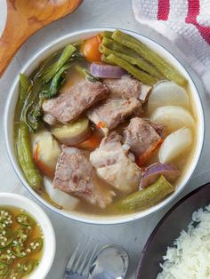 a bowl of soup with meat, vegetables and rice on a table next to a spoon