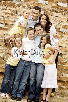 a family posing for a photo in front of a brick wall with their arms around each other