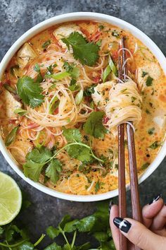 someone is holding chopsticks over a bowl of noodles and cilantro sauce